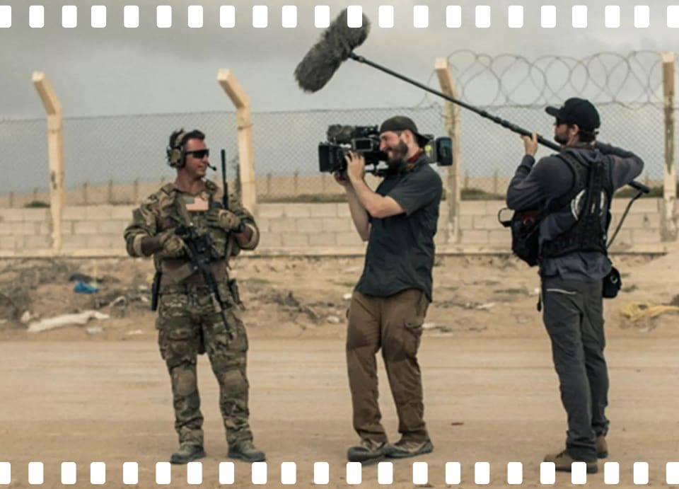 Soldier being filmed by camera crew outside.